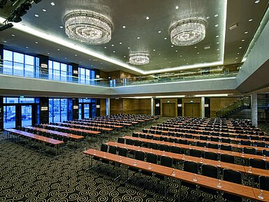 Salón moderno en el Maritim Hotel Düsseldorf con asientos en fila, grandes ventanas y lámparas de araña impresionantes.