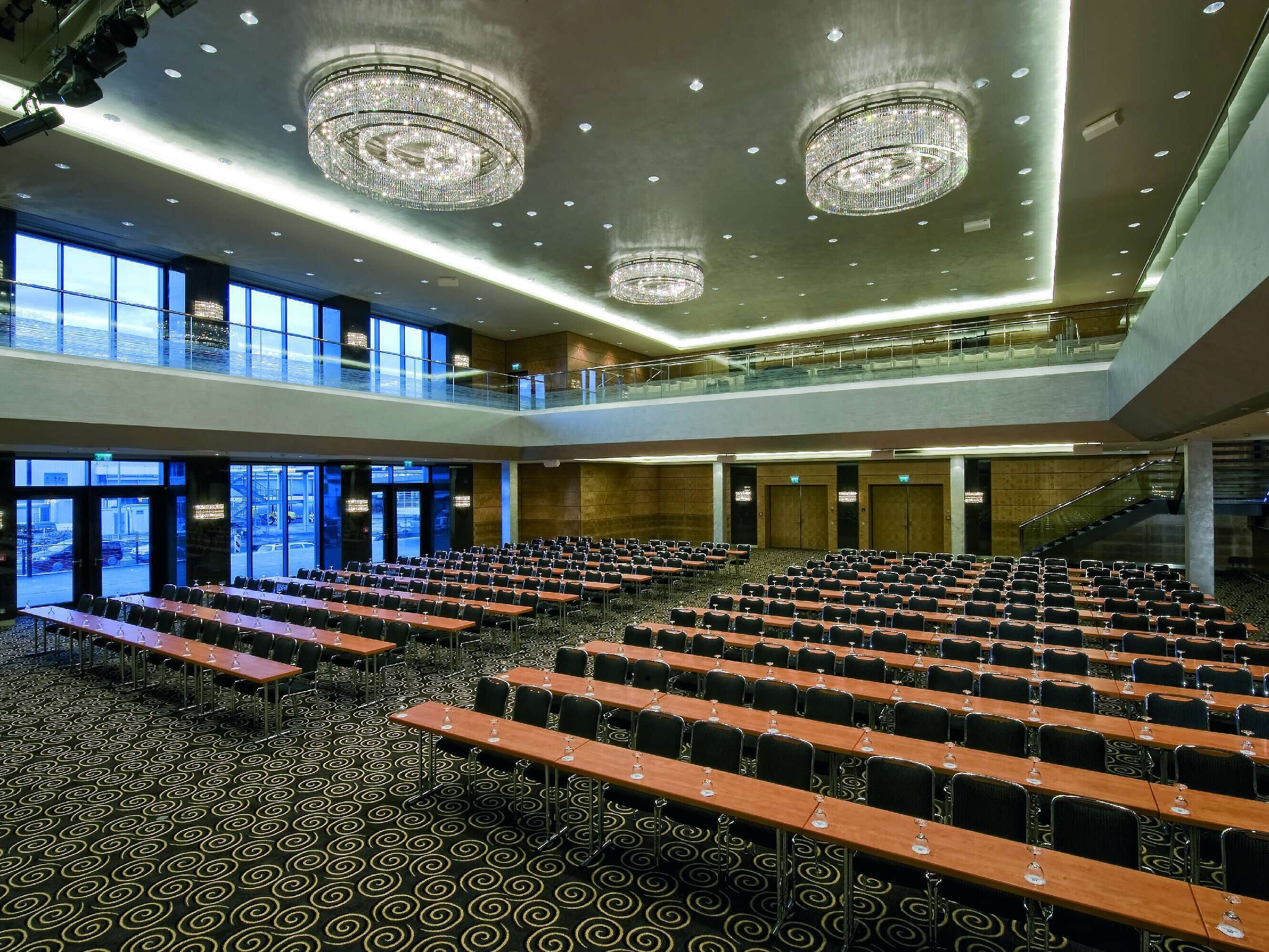 Salón moderno en el Maritim Hotel Düsseldorf con asientos en fila, grandes ventanas y lámparas de araña impresionantes.