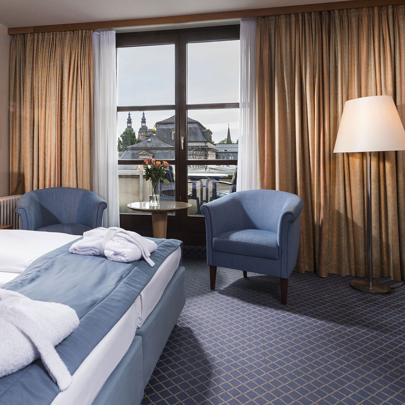 Elegante camera Superior al Maritim Hotel Fulda con letto matrimoniale, area salotto e balcone con vista sulla città.