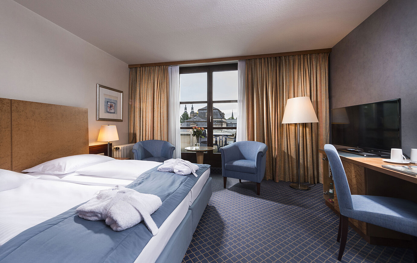 Elegante camera Superior al Maritim Hotel Fulda con letto matrimoniale, area salotto e balcone con vista sulla città.