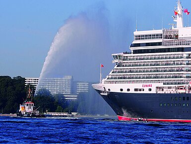 Exterior view of the Maritim Hotel Kiel, in the foreground the cruise ship Queen Elizabeth and a tugboat on the water.