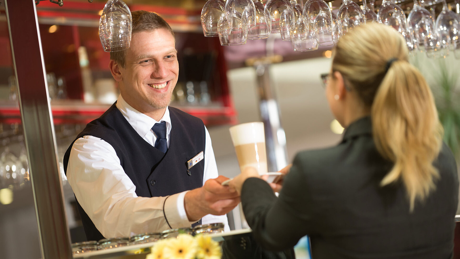 A bartender handing a drink to a guest at the bar in Maritim Hotel with a friendly smile