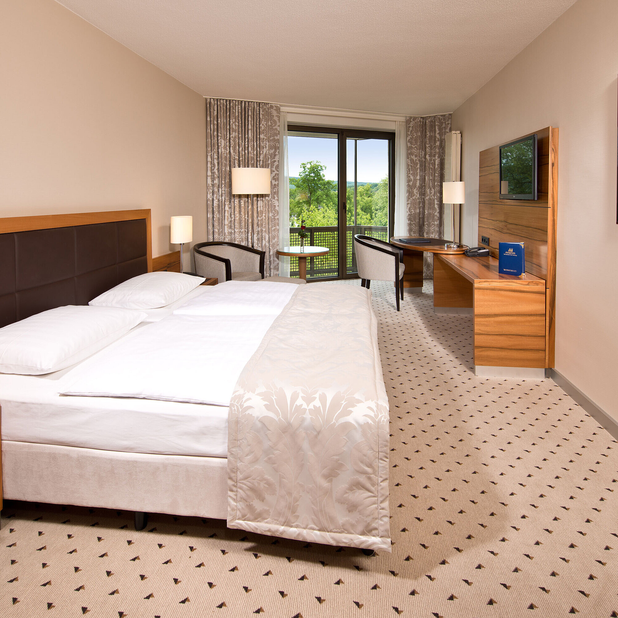Bright room at Maritim Hotel Bad Homburg with cozy bed, desk, and balcony with green view.