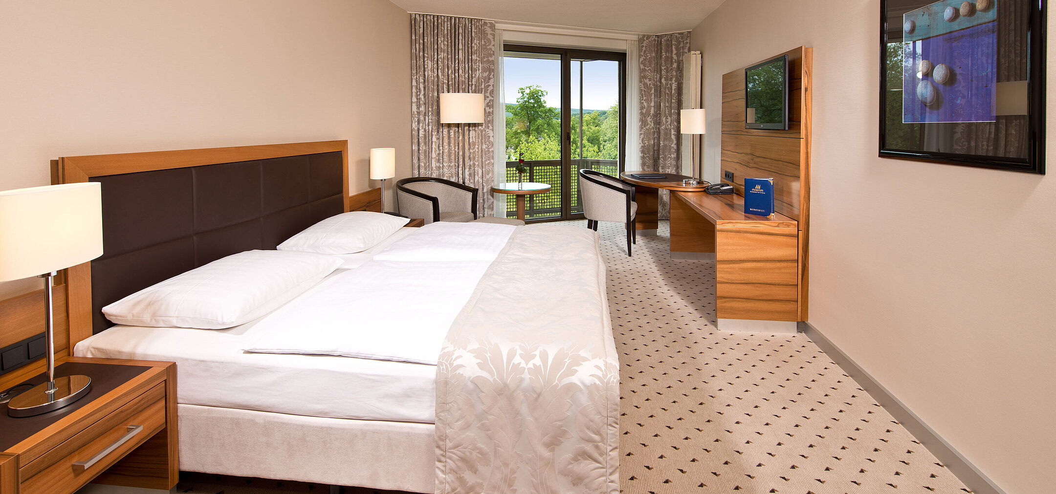 Camera luminosa all'hotel Maritim Bad Homburg con letto accogliente, scrivania e balcone con vista sul verde.