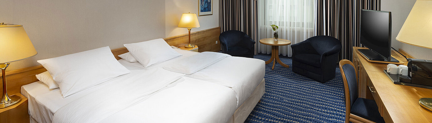 Large bed with bedside tables and lamps, next to seating area and desk.