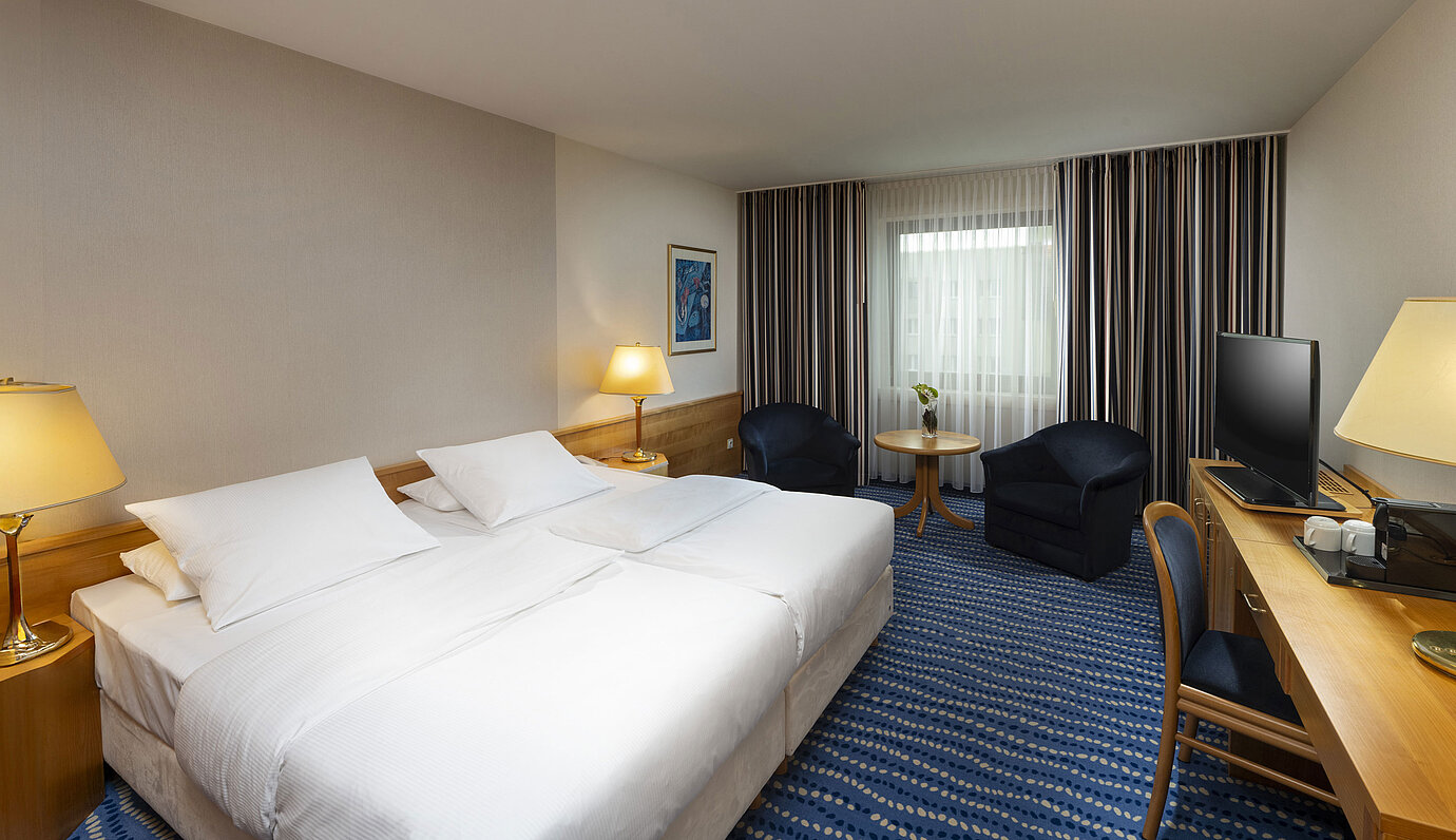 Large bed with bedside tables and lamps, next to seating area and desk.