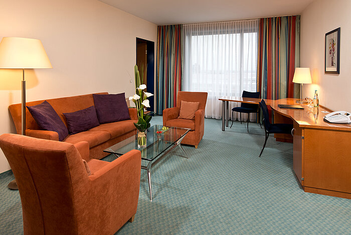 Suite junior spacieuse à l'hôtel Maritim Frankfurt avec coin salon confortable, bureau et éclairage chaleureux.