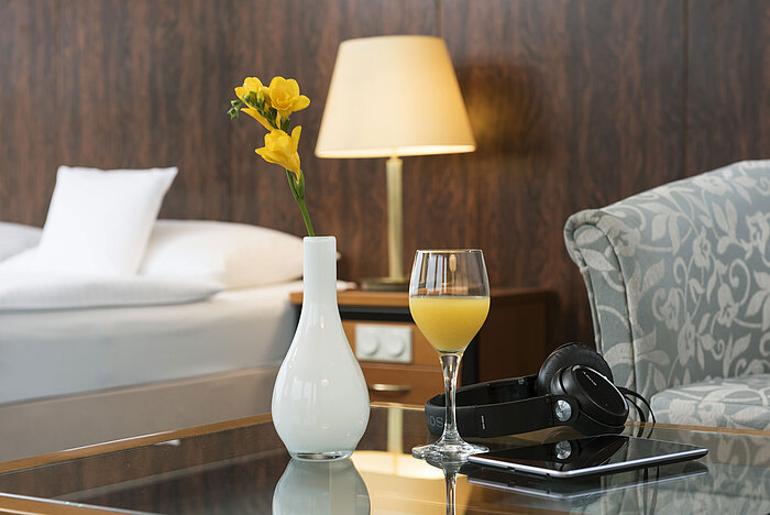 Detalle de la sala Dettagli di una camera del Maritim Hotel Kiel: bicchiere di succo d'arancia, cuffie e vaso sul tavolo, letto sullo sfondo.