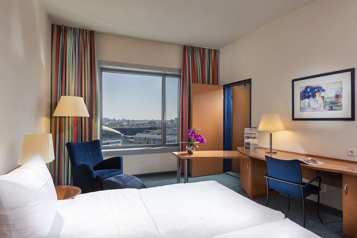 Chambre familiale Confort du Maritim Hotel Frankfurt avec lit double, bureau, rideaux colorés et vue sur la ville.