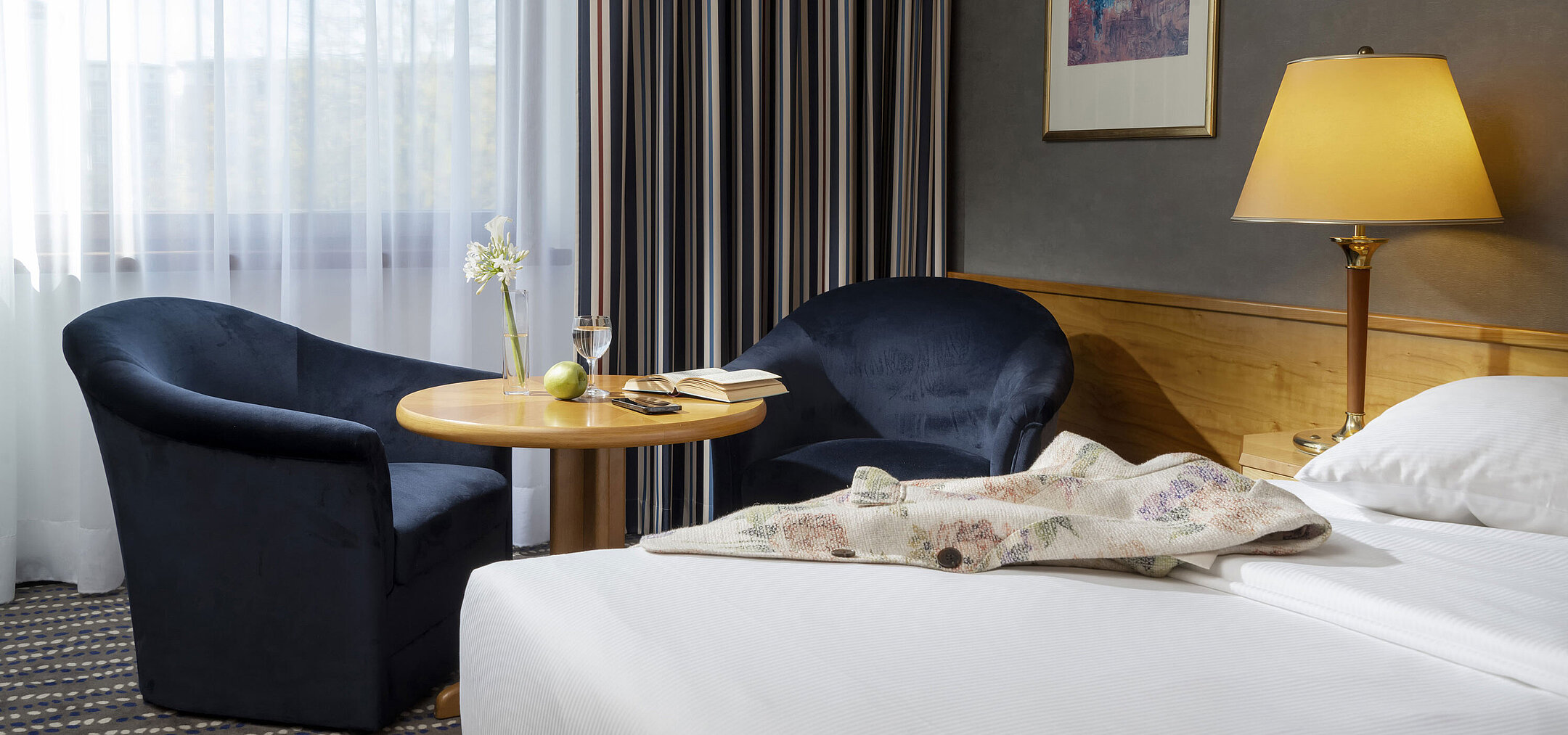 Area salotto in camera d'hotel con tavolo, libro, bicchiere d'acqua e mela, perfetta per rilassarsi