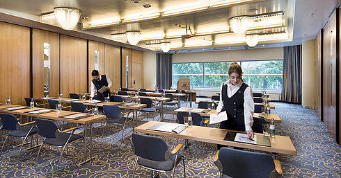El personal prepara una sala de conferencias en el Maritim Hotel Frankfurt con sillas en fila y vistas al verde.