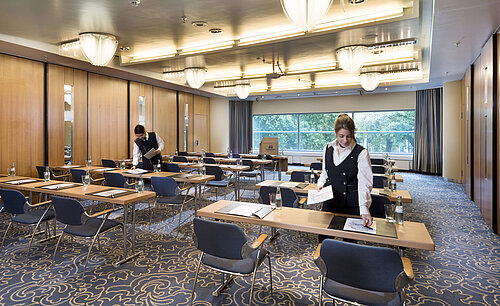 Il personale prepara una sala conferenze al Maritim Hotel Frankfurt con posti a sedere in fila e vista sul verde.