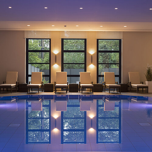 Área de piscina del Hotel Maritim Bonn con elegantes tumbonas e iluminación calmante para una relajación total.