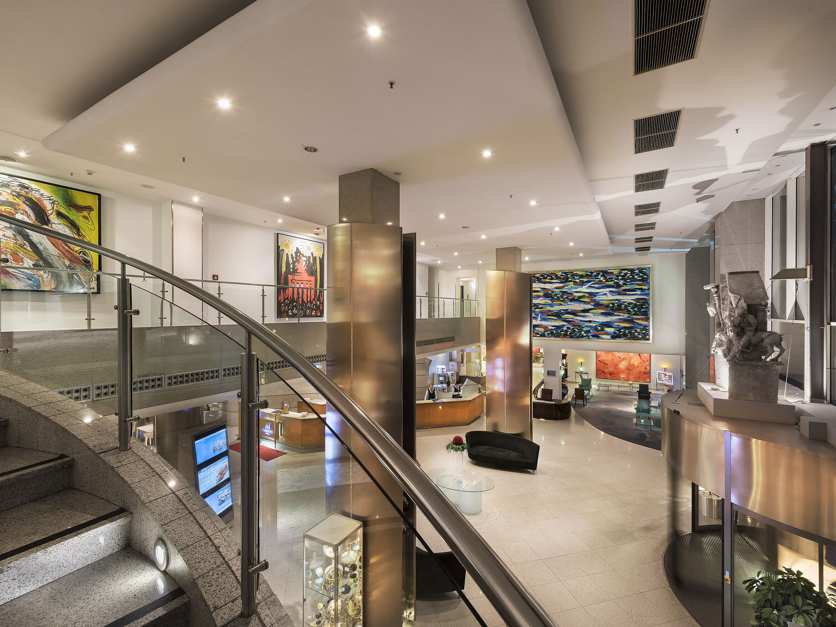 Ampia hall moderna del Maritim proArte Hotel con opere d'arte, scala curva e interni eleganti.