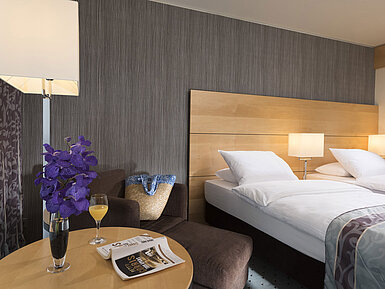 Classic room at Maritim Hotel Düsseldorf with elegant double bed, cozy seating area, fresh flower, and reading material.