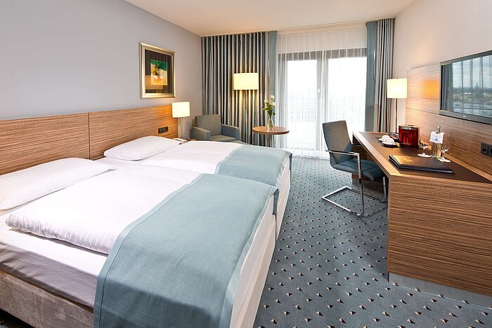 Habitación Superior en el Hotel Maritim Darmstadt con cama doble, escritorio, zona de estar y vista al balcón.