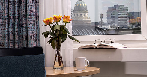 Jarrón con rosas amarillas, libro y taza junto a la ventana con vistas al Domo Francés en Maritim proArte Hotel