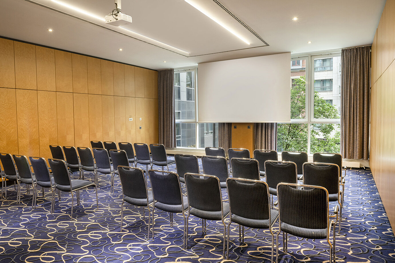 Salle de conférence moderne au Maritim proArte Hotel Berlin avec rangées de chaises et écran.