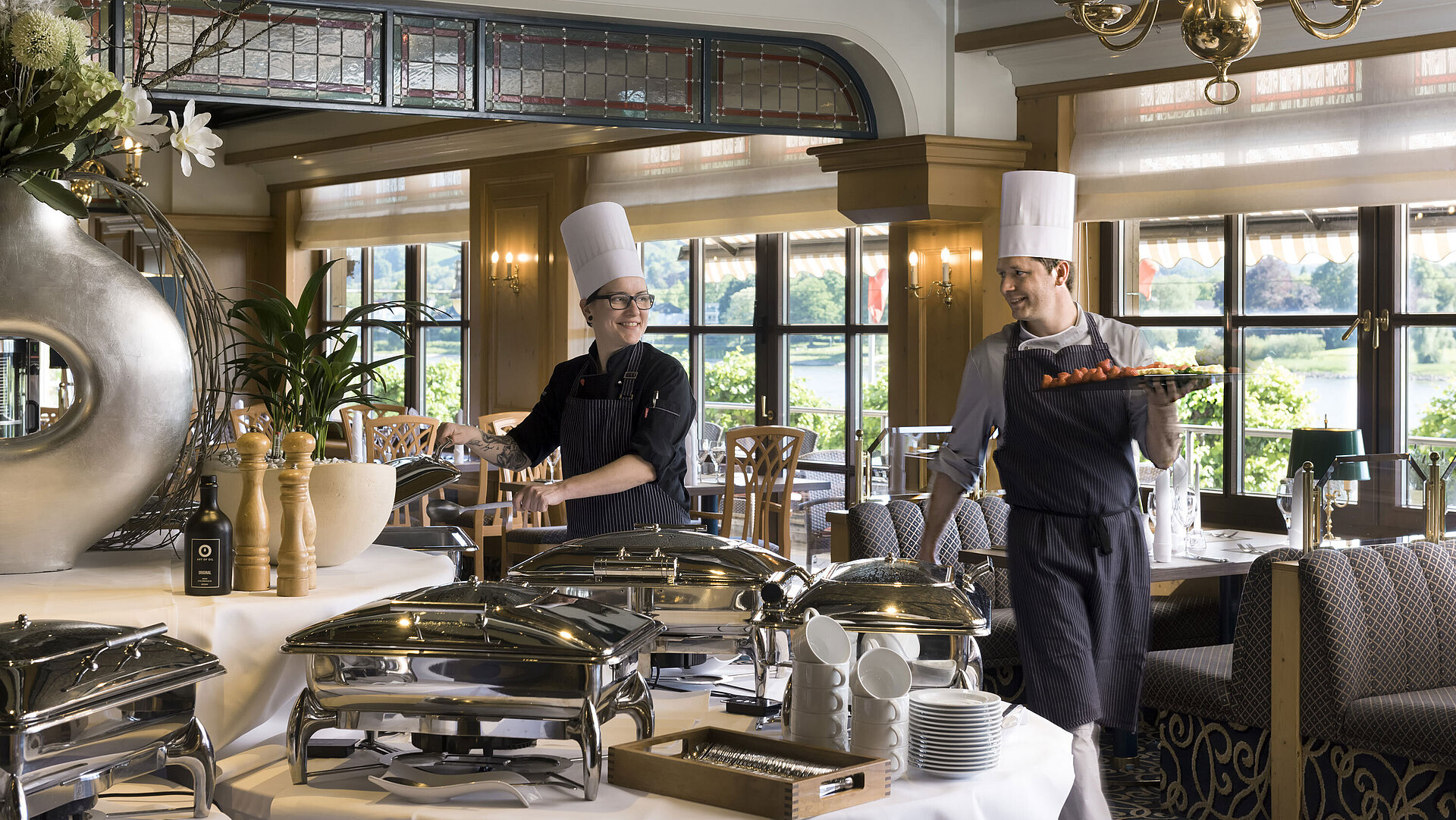 Deux chefs au buffet du Maritim Hotel Königswinter préparent des plats fraîchement disposés avec vue sur le Rhin.
