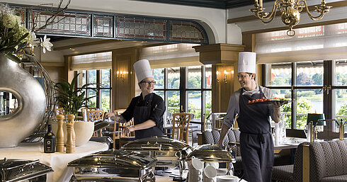 Dos chefs en el buffet del Maritim Hotel Königswinter preparando platos frescos con vista al Rin.