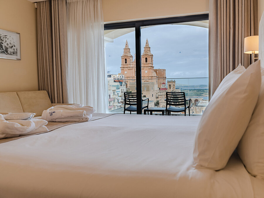 Camera d’hotel con letto matrimoniale, balcone e vista su chiesa storica e città