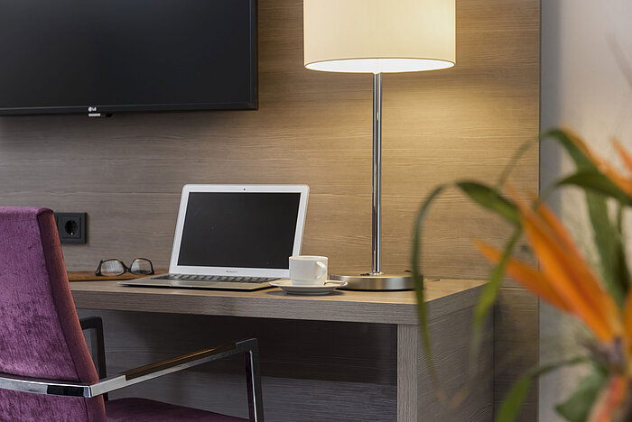 Escritorio del Maritim Hotel Königswinter con laptop, gafas y lámpara elegante.