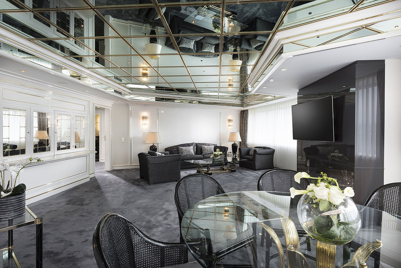 Sala de estar elegante de la suite de lujo del Hotel Maritim Bonn con techo de espejo,muebles modernos y gran mesa de comedor