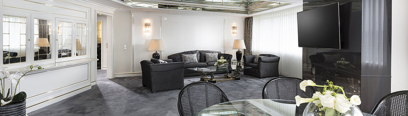 Sala de estar elegante de la suite de lujo del Hotel Maritim Bonn con techo de espejo,muebles modernos y gran mesa de comedor