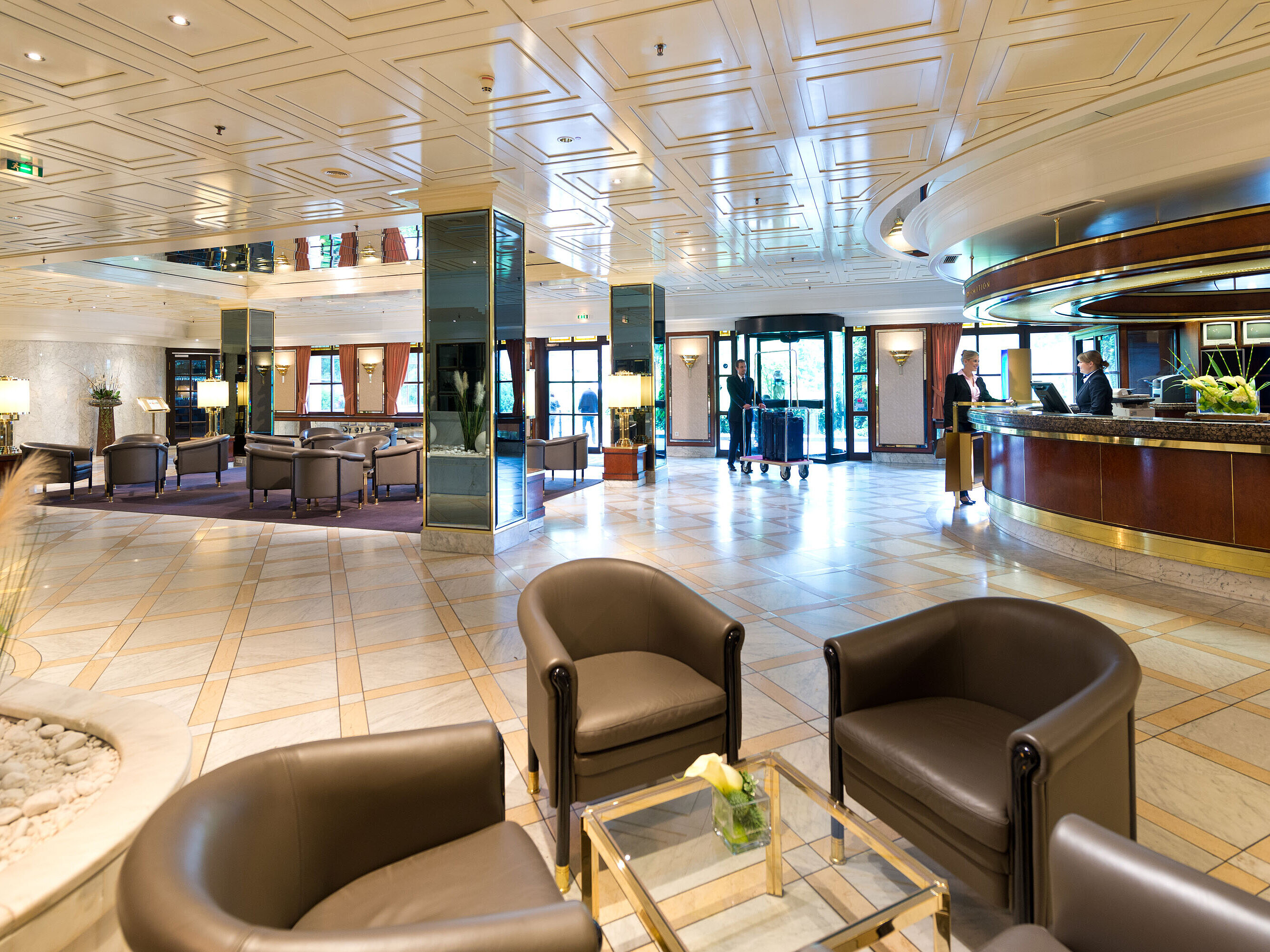 Elegante vestíbulo del Maritim Hotel Königswinter con recepción sofisticada, zonas de descanso y ambiente luminoso.