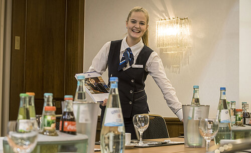 Amable empleado de servicio en el Salón Lenné del Maritim Hotel Bonn con bebidas y documentos de la conferencia sobre la mesa.