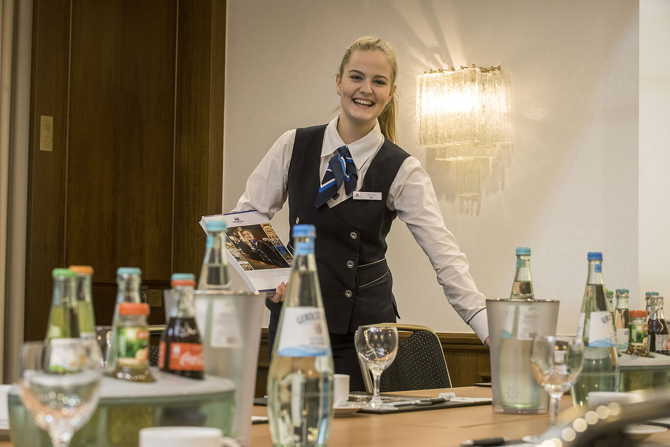 Amable empleado de servicio en el Salón Lenné del Maritim Hotel Bonn con bebidas y documentos de la conferencia sobre la mesa.