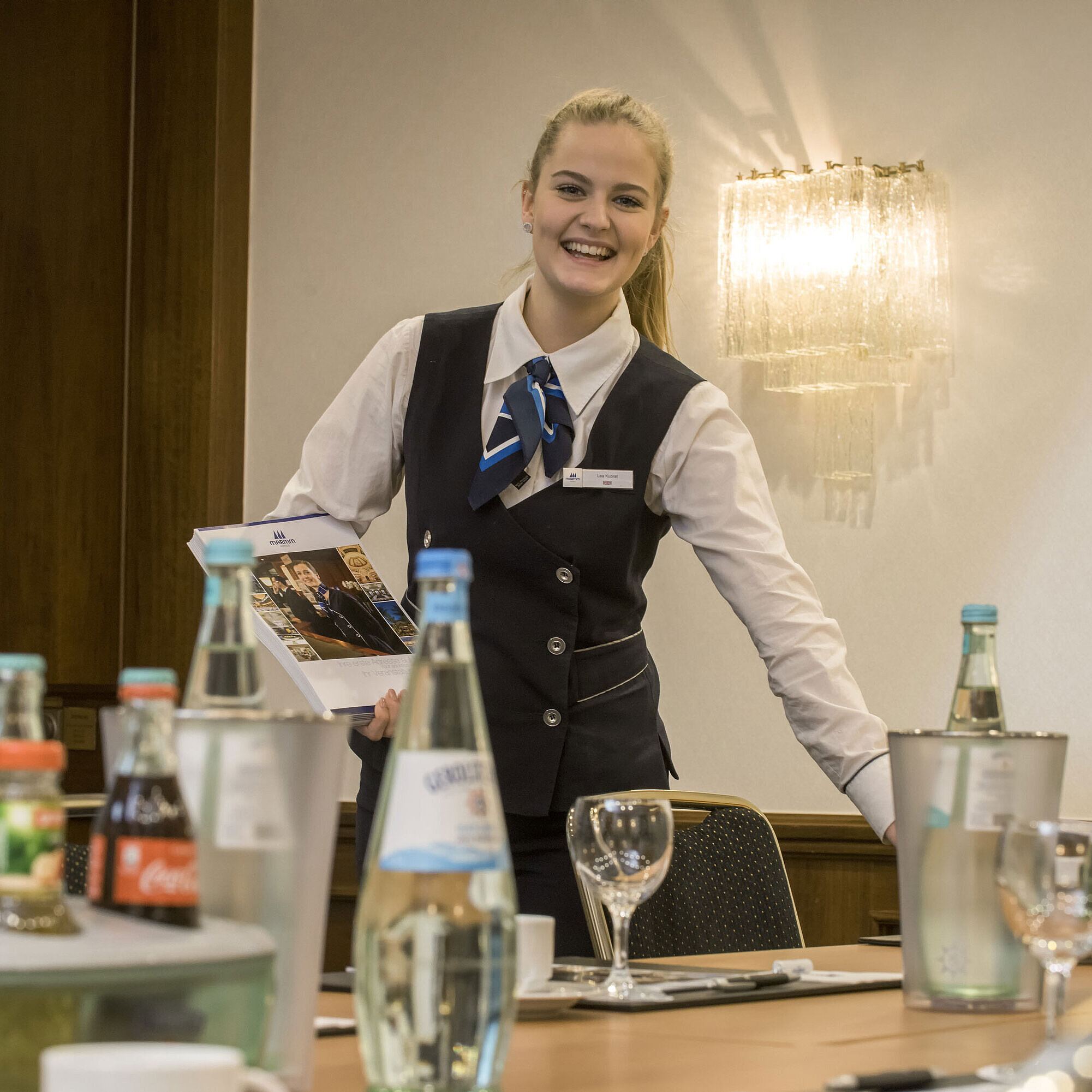 Friendly service employee in the Salon Lenné of the Maritim Hotel Bonn with drinks and conference documents on the table.