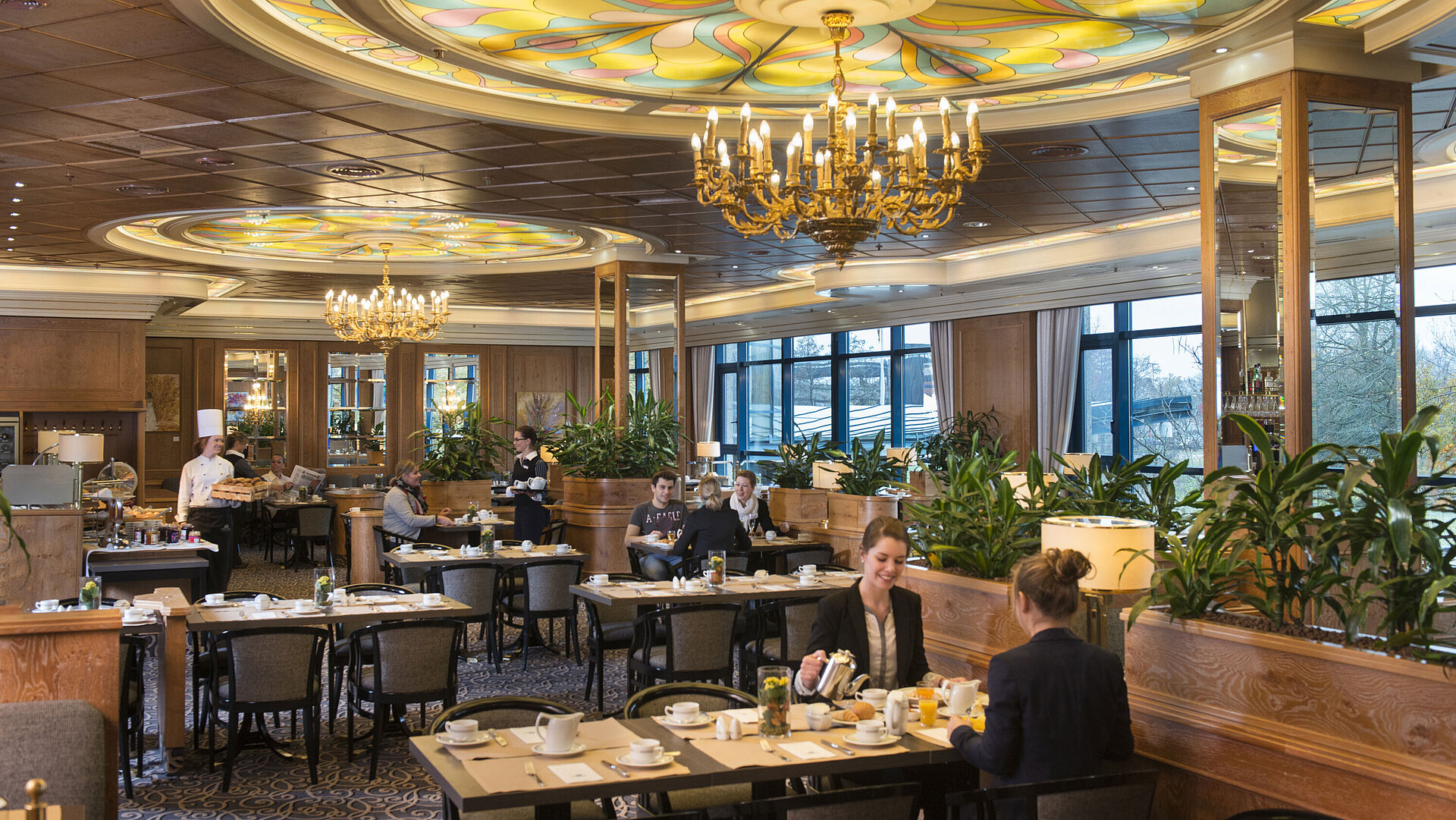 Guests enjoy breakfast in a stylish restaurant with chandeliers and large windows at Maritim Hotel Hannover.