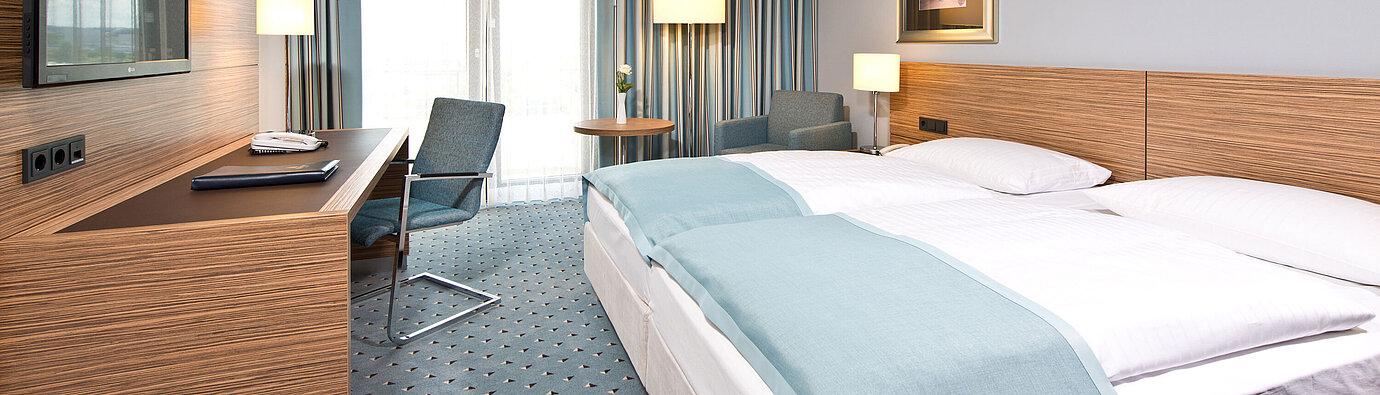 Habitación Comfort en el Maritim Hotel Darmstadt con diseño moderno, escritorio, zona de estar acogedora y grandes ventanas.