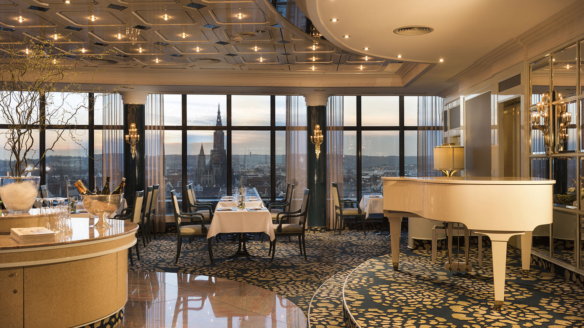Elegant panorama restaurant with grand piano and sunset view of Ulm Minster