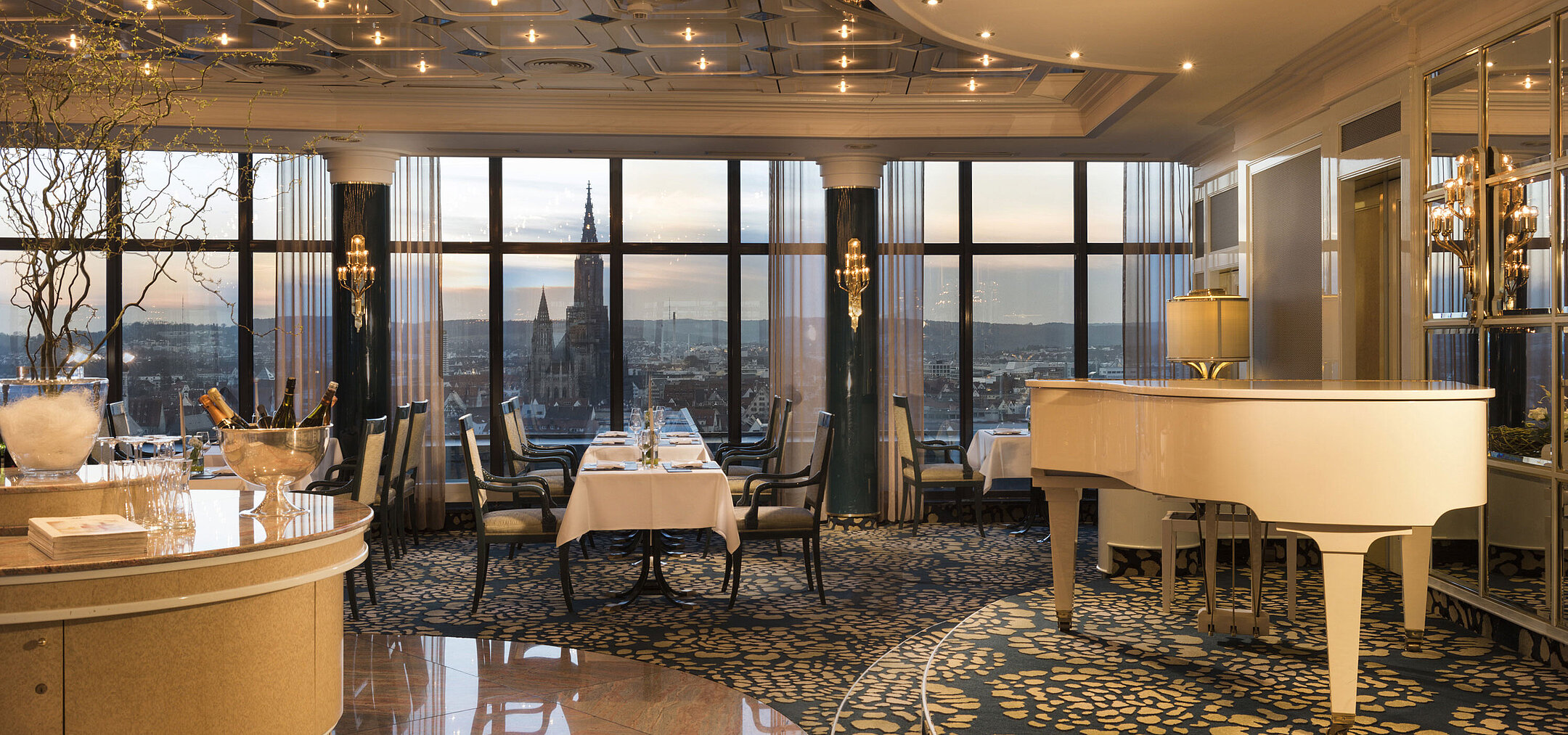 Elegant panorama restaurant with grand piano and sunset view of Ulm Minster