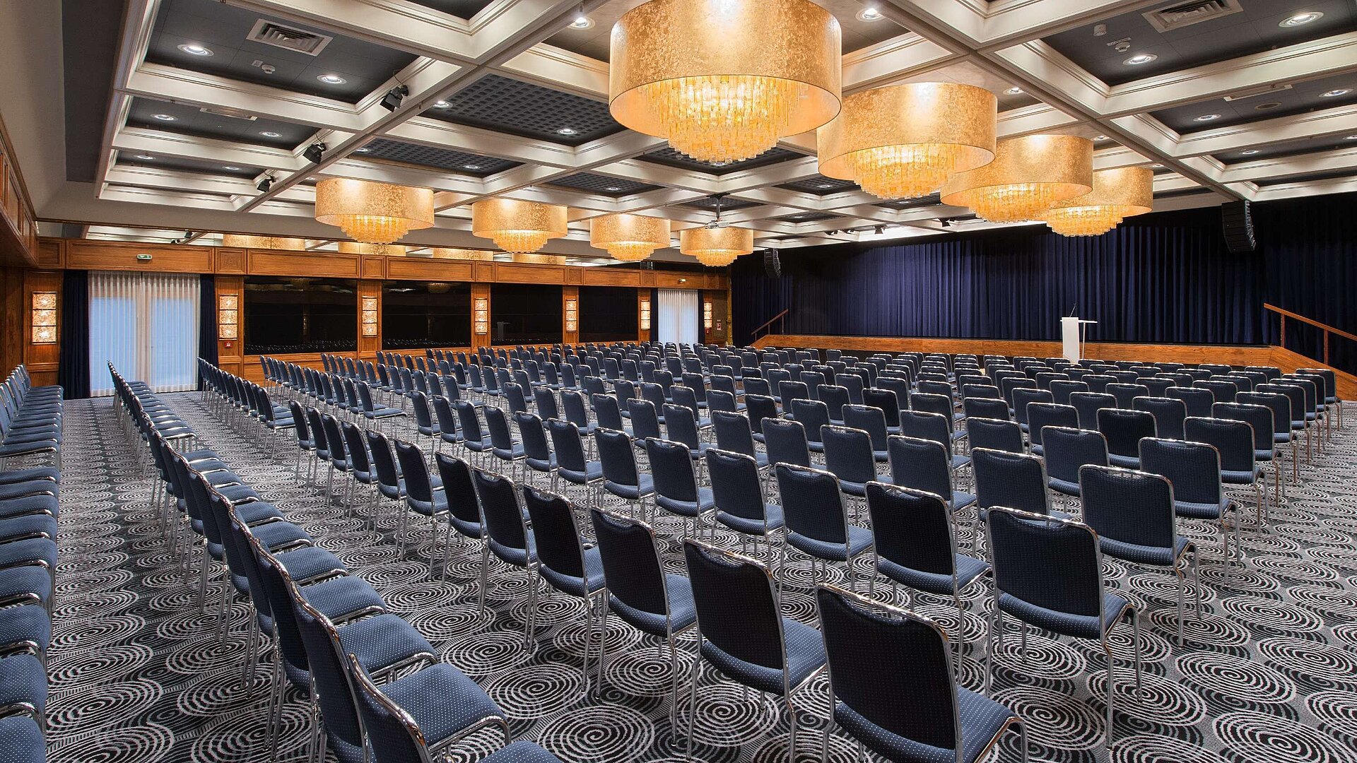 Salón elegante en el Hotel Maritim Darmstadt con asientos en fila, impresionantes lámparas y equipamiento ideal para eventos.
