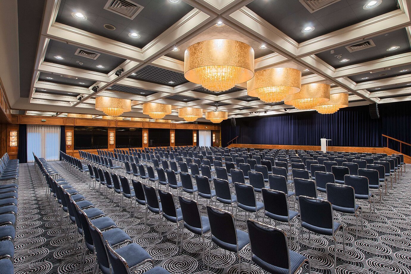 Salón elegante en el Hotel Maritim Darmstadt con asientos en fila, impresionantes lámparas y equipamiento ideal para eventos.