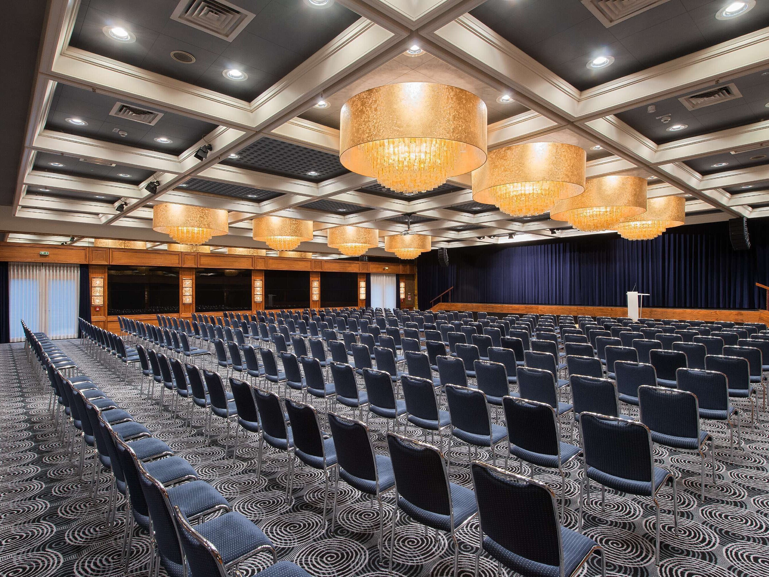 Salón elegante en el Hotel Maritim Darmstadt con asientos en fila, impresionantes lámparas y equipamiento ideal para eventos.
