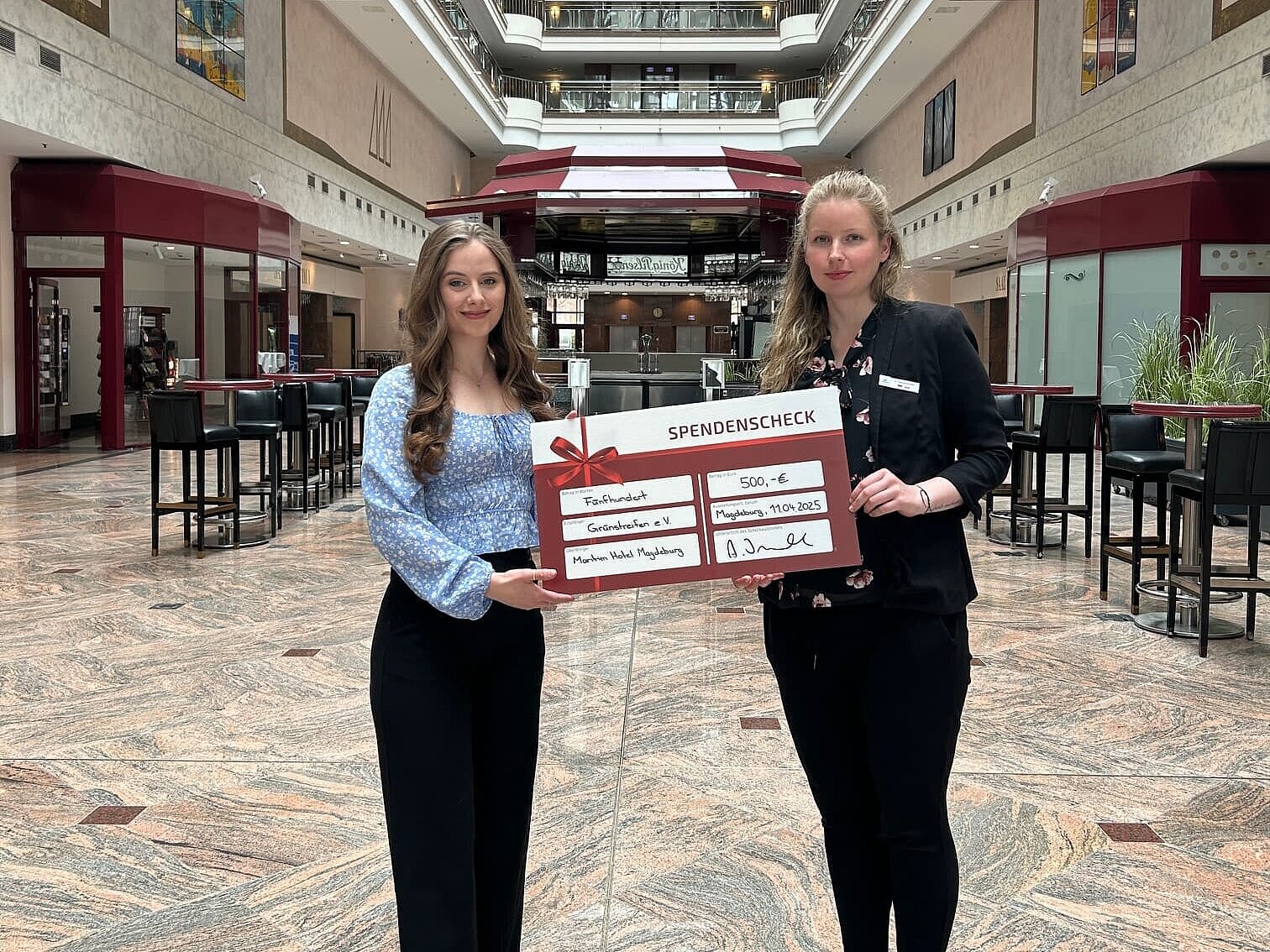 Employees of Maritim Hotel Magdeburg holding a donation cheque in the hotel lobby.