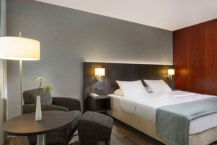 Modern double room at Maritim Hotel Bremen with cozy seating area, side table, vase, and inviting bed.