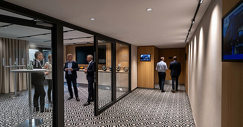 Coffee break area with standing tables, coffee station and guests talking during a conference break.
