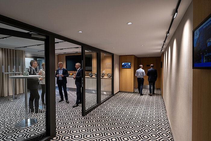 Zona de pausa para café con mesas altas, estación de café y participantes conversando durante el descanso.