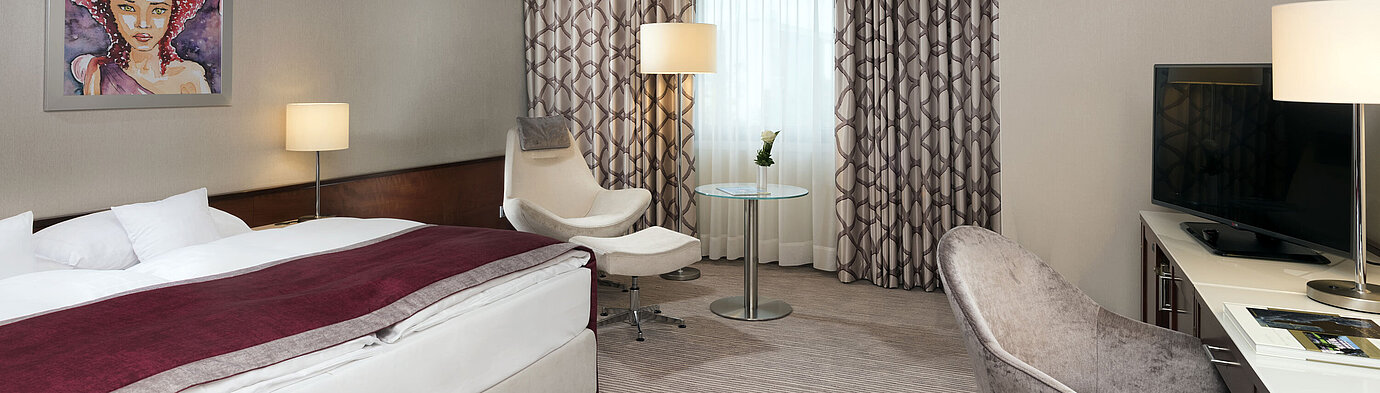 Habitación Comfort en el Hotel Maritim Bonn con cama acogedora, sillas, escritorio y cortinas modernas.