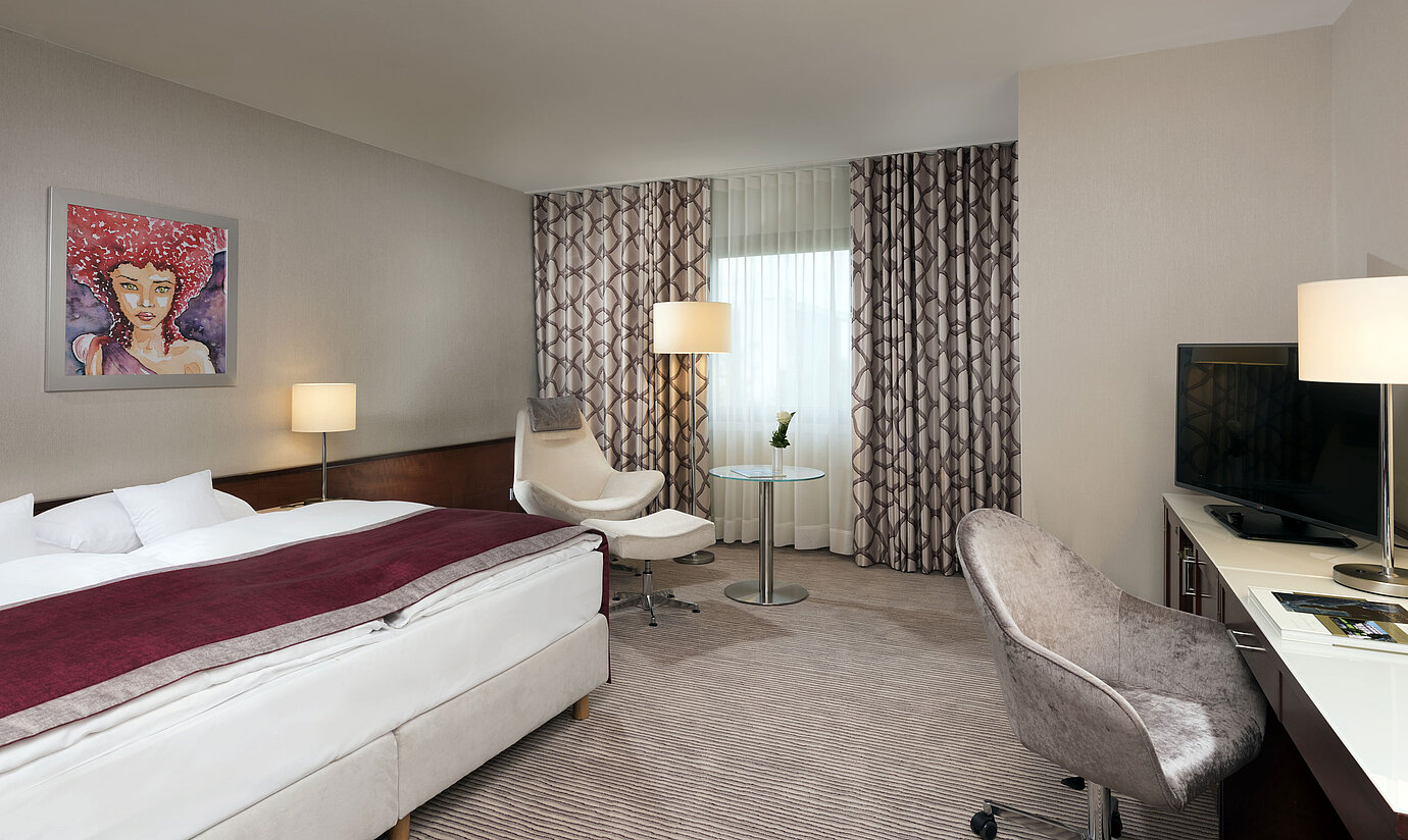 Habitación Comfort en el Hotel Maritim Bonn con cama acogedora, sillas, escritorio y cortinas modernas.