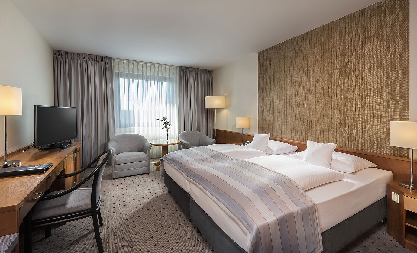 Habitación doble Classic moderna con cama doble acogedora, zona de estar y escritorio en el hotel Maritim Hannover.