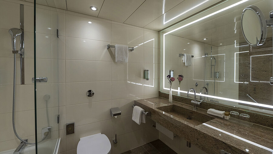 Modern bathroom at Maritim Hotel Bremen with illuminated mirror, bathtub, and high-quality granite surfaces.