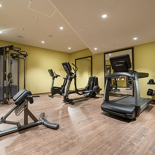 Salle de sport moderne à l'hôtel Maritim Ingolstadt avec tapis de course, haltères et équipements d'entraînement.