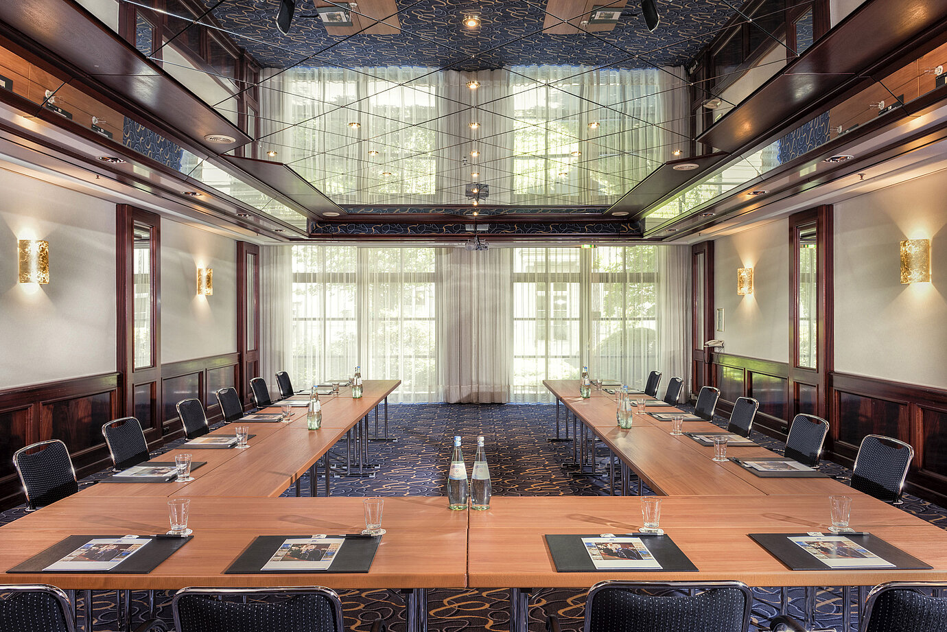 Salle de conférence élégante avec disposition en U, lumière naturelle et plafond miroir.