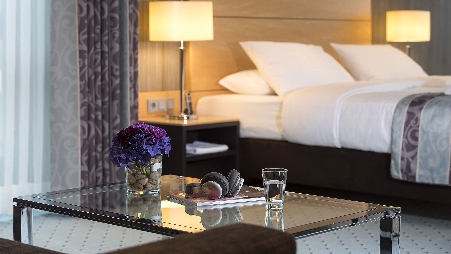 Close-up of the master suite at Maritim Hotel Düsseldorf with a glass, headphones, and flowers on a glass table.